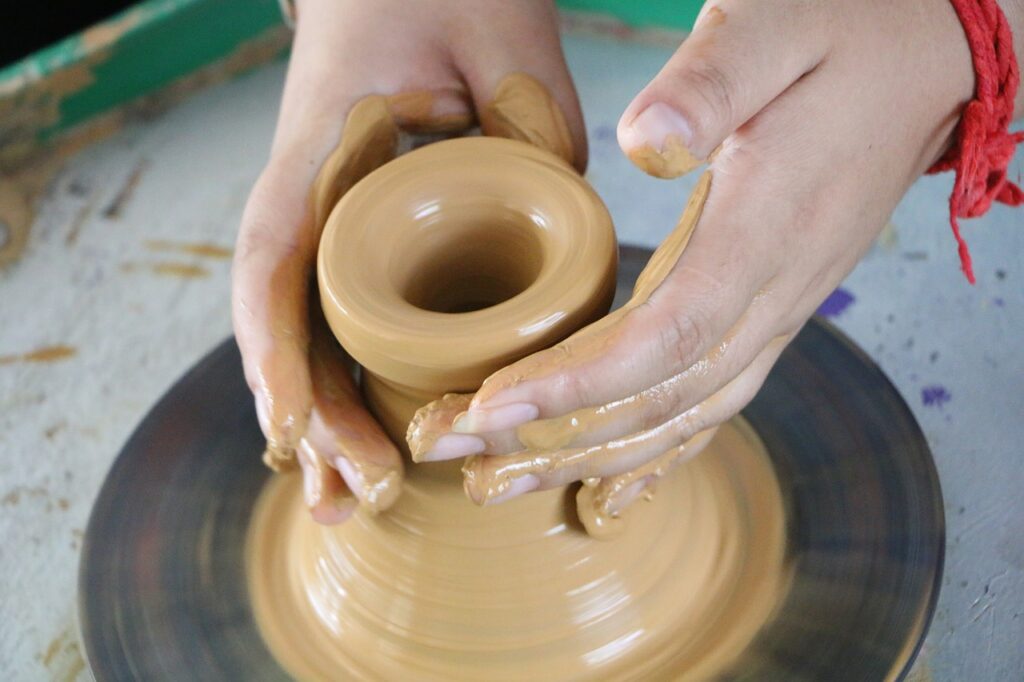 Hands shaping wet clay on a spinning potter's wheel.