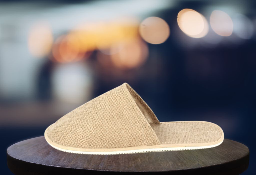 A single beige slipper on a wooden surface against a blurred light background.