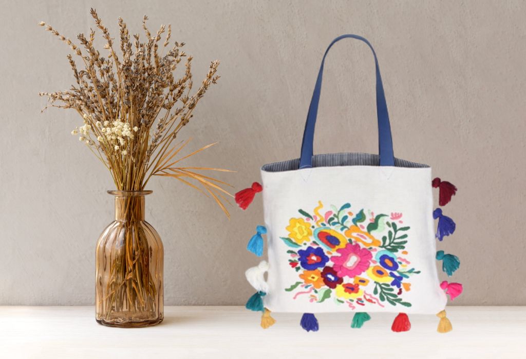 Embroidered tote bag with colorful floral pattern next to a gold-tinted vase with dried flowers.